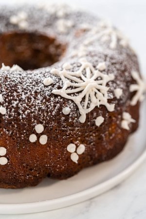 Téléchargez les photos : Gingerbread bundt cake with caramel filling, buttercream frosting, and powdered sugar dusting on the kitchen counter. - en image libre de droit