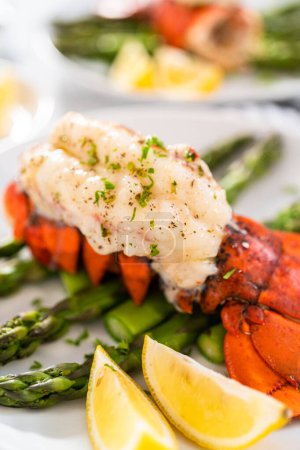 Téléchargez les photos : Servir des queues de homard à l'ail avec des asperges à la vapeur et des quartiers de citron sur une assiette blanche. - en image libre de droit