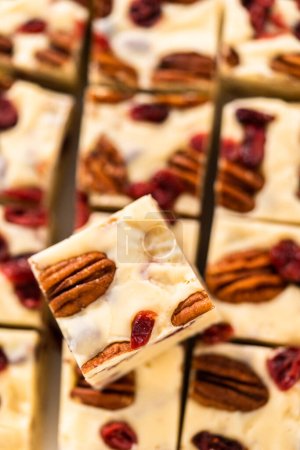 Foto de Corte de chocolate blanco dulce de nuez de arándano en trozos pequeños en una tabla de cortar blanca. - Imagen libre de derechos