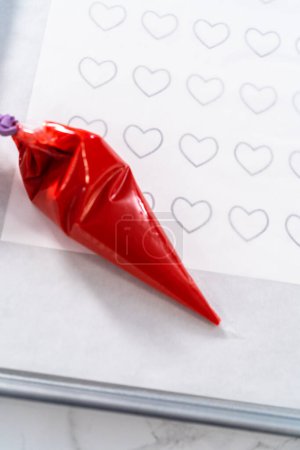 Photo for Piping melted chocolate from piping back over the parchment paper to make a chocolate heart. - Royalty Free Image