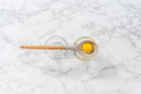Foto de Flat lay. Separating egg whites and egg yolks with slotted spoon into small bowls. - Imagen libre de derechos