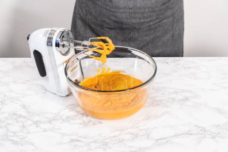 Téléchargez les photos : Mélanger les ingrédients dans un grand bol à mélanger en verre pour faire cuire le gâteau à la citrouille. - en image libre de droit