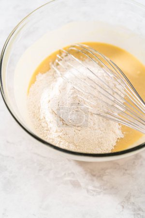 Foto de Mezclar ingredientes húmedos y secos con un batidor de mano en un tazón de vidrio para hornear un pastel de zanahoria con glaseado de queso crema. - Imagen libre de derechos
