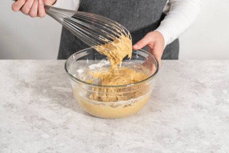 Foto de Mixing ingredients with a hand whisk in a large mixing bowl to bake banana cookies with chocolate drizzle. - Imagen libre de derechos