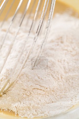 Foto de Mezclar ingredientes húmedos y secos con un batidor de mano en un tazón de vidrio para hornear magdalenas de semillas de amapola de limón. - Imagen libre de derechos