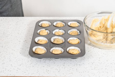 Photo for Scooping cupcake batter with dough scoop into a baking cupcake pan with liners to bake dulce de leche cupcakes. - Royalty Free Image