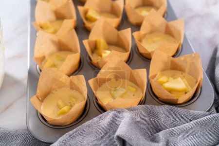 Photo for Scooping dough into the cupcake pan lined with parchment muffin liners to bake sharlotka muffins. - Royalty Free Image