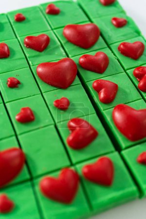 Téléchargez les photos : Pose plate. Caramel vert fait maison avec des morceaux carrés de cœurs rouges sur un comptoir de cuisine. - en image libre de droit