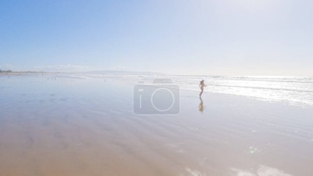 Photo for Little girl, braving the cold, joyfully runs in her swimsuit across the beach during winter. - Royalty Free Image