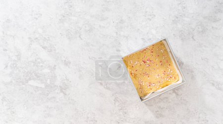 Téléchargez les photos : Pose plate. Remplissage carré moule à gâteau au fromage doublé de papier parchemin avec mélange de caramel pour préparer le caramel à la canne à sucre. - en image libre de droit
