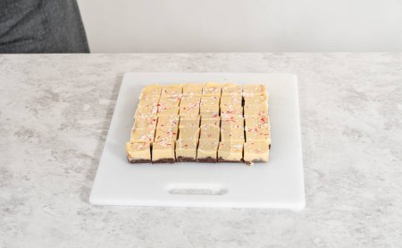 Photo for Cutting candy cane fudge with a large kitchen knife into square pieces on a white cutting board. - Royalty Free Image