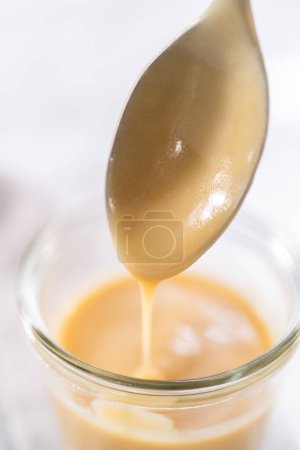 Téléchargez les photos : Glaçage au caramel fait maison dans un bocal en verre sur le comptoir de la cuisine. - en image libre de droit