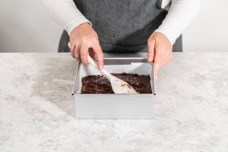 Photo for Filling square cheesecake pan lined with parchment paper with fudge mixture to prepare chocolate hazelnut fudge. - Royalty Free Image