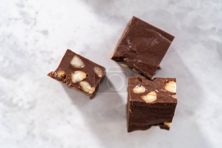 Téléchargez les photos : Chocolat maison macadamia morceaux carrés de caramel sur un comptoir de cuisine. - en image libre de droit