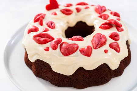 Téléchargez les photos : Freshly baked red velvet bundt cake with chocolate lips and hearts over cream cheese glaze for Valentines Day. - en image libre de droit