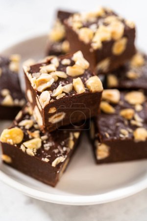 Téléchargez les photos : Pièces carrées de caramel aux noisettes au chocolat maison sur une assiette blanche. - en image libre de droit