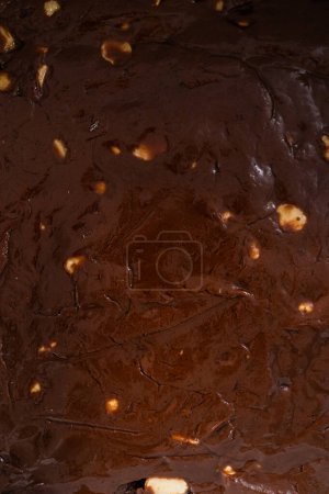 Photo for Filling square cheesecake pan lined with parchment paper with fudge mixture to prepare chocolate macadamia fudge. - Royalty Free Image