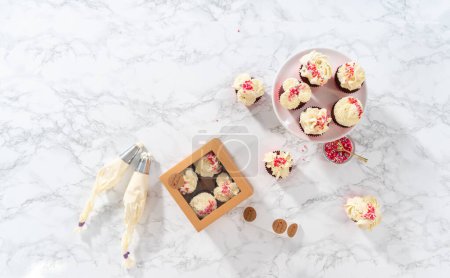 Téléchargez les photos : Pose plate. Emballage fraîchement cuit cupcakes en velours rouge avec glaçage ganache au chocolat blanc dans la boîte à cupcakes. - en image libre de droit