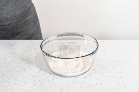 Foto de Mezclar los ingredientes secos con un batidor de mano en un tazón de vidrio grande para hornear bañadores de naan. - Imagen libre de derechos