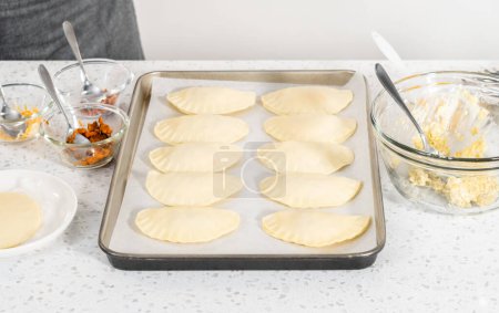Téléchargez les photos : Brosser les empanadas de petit déjeuner non cuites avec des œufs et des patates douces avec le lavage des œufs. - en image libre de droit