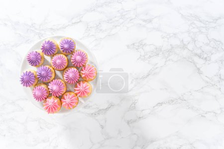 Téléchargez les photos : Pose plate. Mini cupcakes à la vanille fraîchement cuits avec glaçage beurre rose ombre sur un stand de gâteau blanc. - en image libre de droit