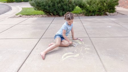 Photo for Little girl drawing chalk art on a suburban driveway on a summer day. - Royalty Free Image