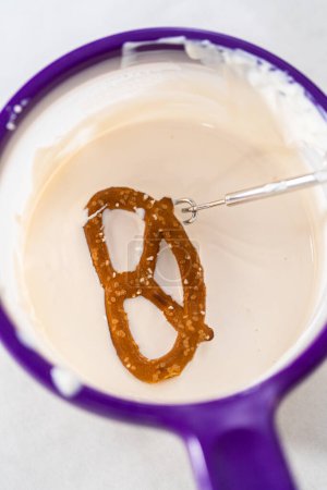 Photo for Dipping pretzels twists into melted chocolate to make chocolate-covered pretzel twists. - Royalty Free Image