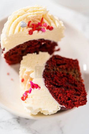 Téléchargez les photos : Cupcakes en velours rouge tranchés avec glaçage ganache au chocolat blanc sur une assiette blanche. - en image libre de droit