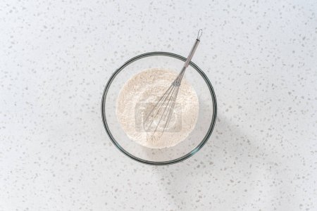 Foto de Acostado. Mezclar los ingredientes secos con un batidor de mano en un tazón de vidrio grande para hornear bañadores de naan. - Imagen libre de derechos