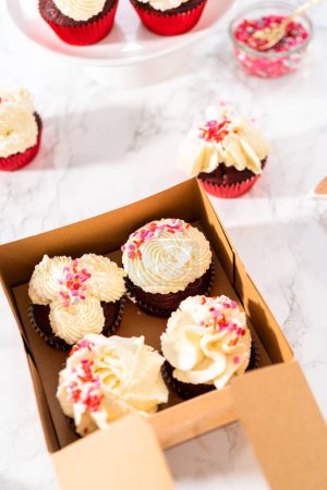 Téléchargez les photos : Emballage fraîchement cuit cupcakes en velours rouge avec glaçage ganache au chocolat blanc dans la boîte à cupcakes. - en image libre de droit