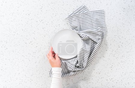 Foto de Acostado. Vacíe un plato blanco con una toalla de cocina en el mostrador de cocina blanco. - Imagen libre de derechos