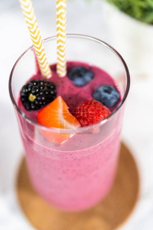 Foto de Freshly made mixed berry smoothie garnished with fresh berries and paper straws. - Imagen libre de derechos