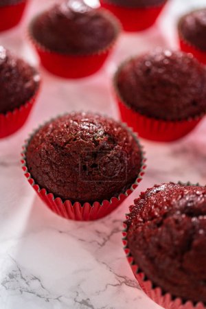 Foto de Enfriamiento recién horneado cupcakes de terciopelo rojo en un mostrador de cocina. - Imagen libre de derechos