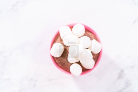 Téléchargez les photos : Remplissage en coquilles de chocolat rose avec mélange de chocolat chaud et mini guimauves pour préparer des bombes au chocolat chaud. - en image libre de droit