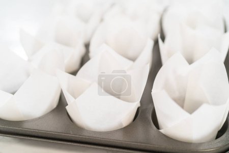 Photo for Lining baking cupcake pan with paper tulip liners to bake no-yeast cinnamon roll cupcakes. - Royalty Free Image