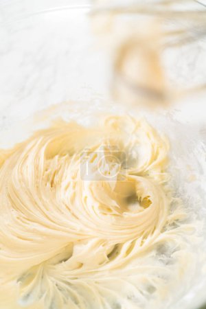 Photo for Mixing ingredients in a glass mixing bowl to make the cream cheese frosting for no-yeast cinnamon roll cupcakes. - Royalty Free Image