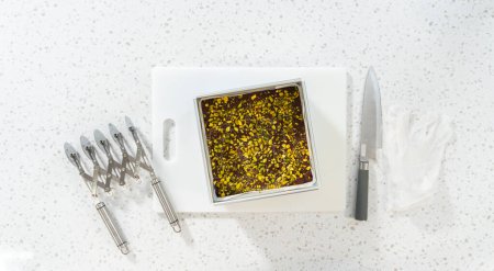 Téléchargez les photos : Flat lay. Removing chocolate pistachio fudge from a square cheesecake pan lined with parchment. - en image libre de droit