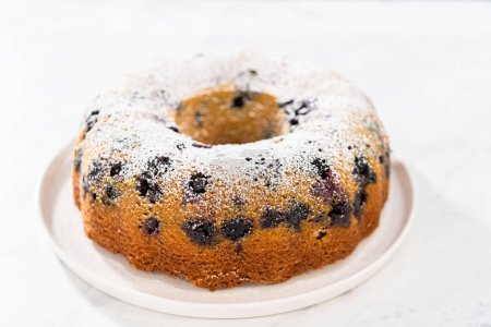 Téléchargez les photos : Saupoudrer le gâteau de lapin de myrtille au citron fraîchement cuit avec du sucre en poudre. - en image libre de droit