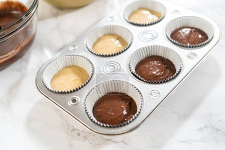 Photo for Cupcake foil liners are being meticulously filled with both chocolate and vanilla batter, setting the stage for the baking of deliciously diverse birthday cupcakes. - Royalty Free Image
