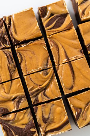 Photo for Cutting chocolate fudge with peanut butter swirl into small pieces on a white cutting board. - Royalty Free Image