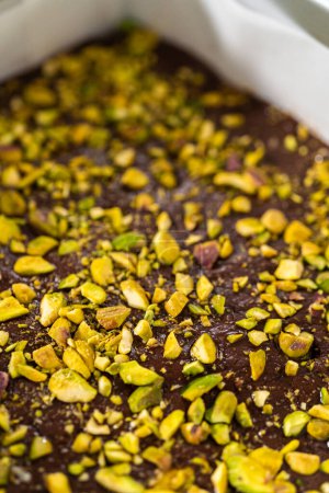 Photo for Filling square cheesecake pan lined with parchment paper with fudge mixture to prepare chocolate pistachio fudge. - Royalty Free Image