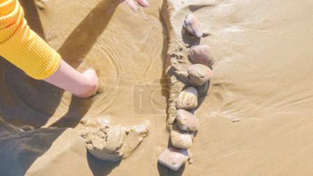 Téléchargez les photos : Petite fille clamant joyeusement sur Pismo Beach, groupée pour le froid hivernal alors qu'elle explore les sables pour les coquillages et les palourdes. - en image libre de droit