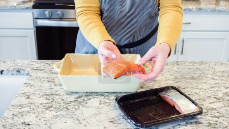 Foto de En una cocina blanca moderna, el salmón crudo se coloca en un plato de cocción de cerámica como parte de la preparación para hornear salmón teriyaki.. - Imagen libre de derechos