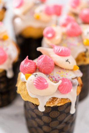 Photo for Freshly baked mini Easter bread kulich with lemon glaze, decorated with sprinkles and meringue bird-shaped cookies. - Royalty Free Image