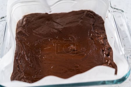 Téléchargez les photos : Verser le mélange de caramel dans le moule tapissé de papier sulfurisé pour préparer le caramel au chocolat avec tourbillon de beurre d'arachide. - en image libre de droit