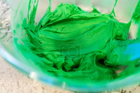 Téléchargez les photos : Dans une cuisine bien éclairée, un assortiment de glaçage à la crème au beurre dans différentes nuances de vert et d'autres couleurs est méticuleusement mélangé et préparé pour la décoration artistique de cupcakes de charme - en image libre de droit