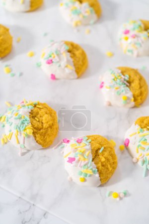 Téléchargez les photos : Biscuits au citron au chocolat blanc. Tremper les biscuits au citron dans du chocolat blanc fondu et les décorer avec des aspersions de Pâques. - en image libre de droit