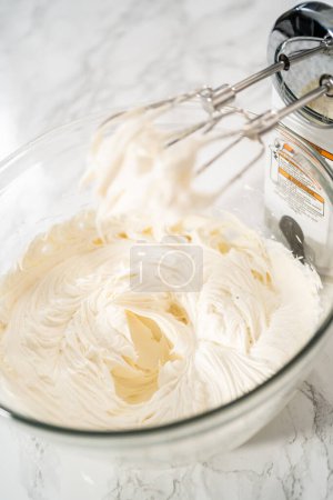 Téléchargez les photos : Fouetter le glaçage à la crème au beurre dans un bol à mélanger en verre avec un mélangeur électrique pour préparer le glaçage à la crème au beurre à la menthe poivrée. - en image libre de droit