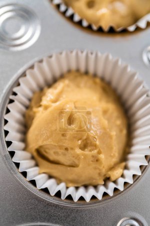Téléchargez les photos : Scooping pâte cupcake avec cuillère à pâte dans une casserole cupcake cuisson avec doublures pour cuire dulce de leche cupcakes. - en image libre de droit