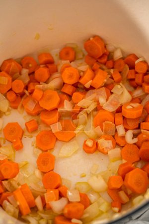 Foto de Salteando verduras en horno holandés esmaltado de hierro fundido para cocinar sopa de guisantes partida. - Imagen libre de derechos